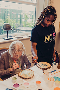 Volunteer from NCS Young People painting with an older lady at Borough Care’s Lisburne Court  